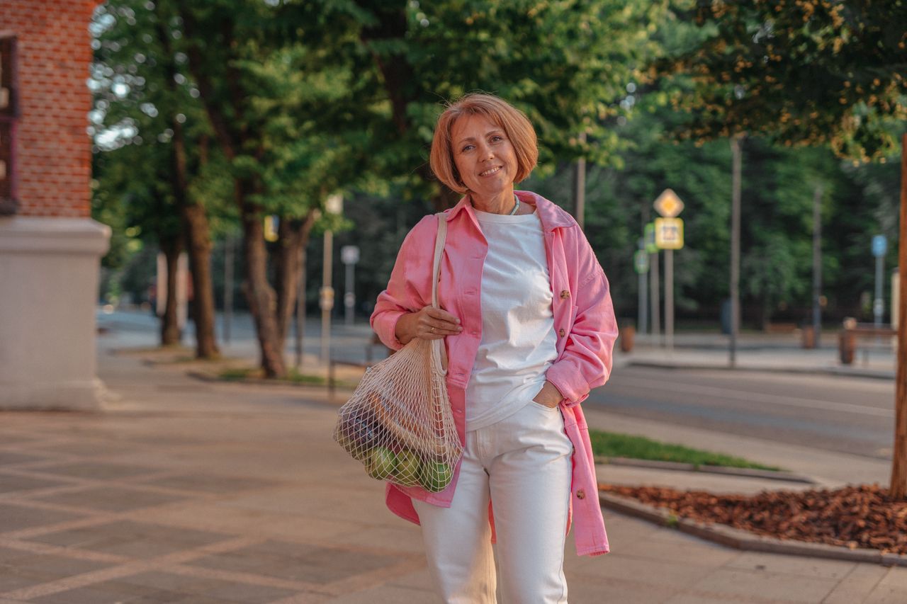 Woman in pink jacket walking on a quiet tree-lined street in a small town