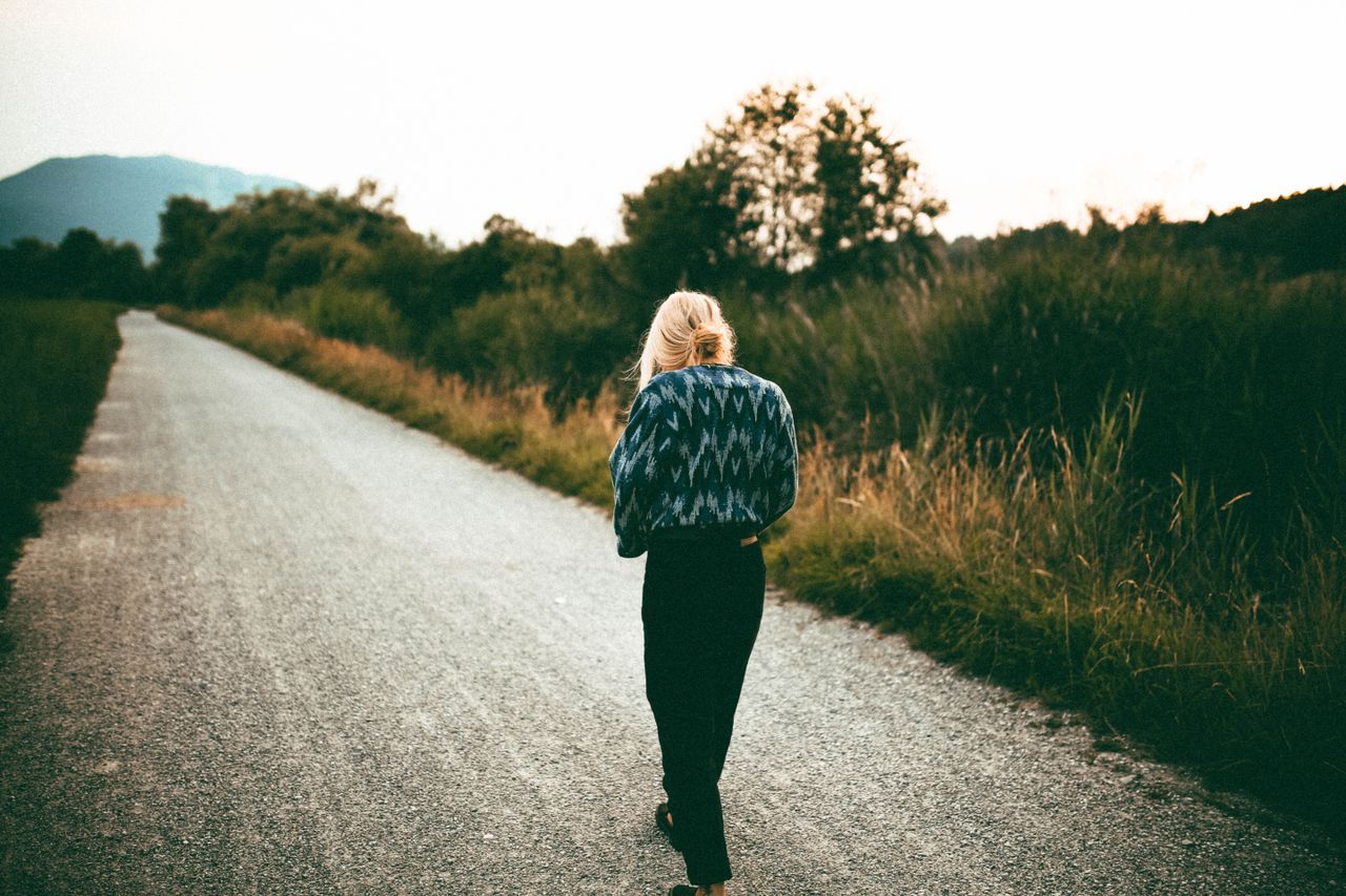 Woman walking alone on a quiet rural path at dusk, seen from behind