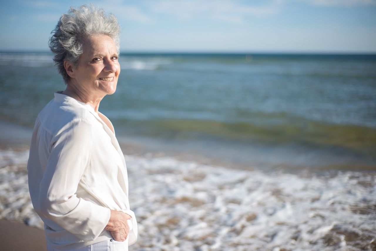 Gray-haired woman in a white blouse standing at the seaside on a sunny day