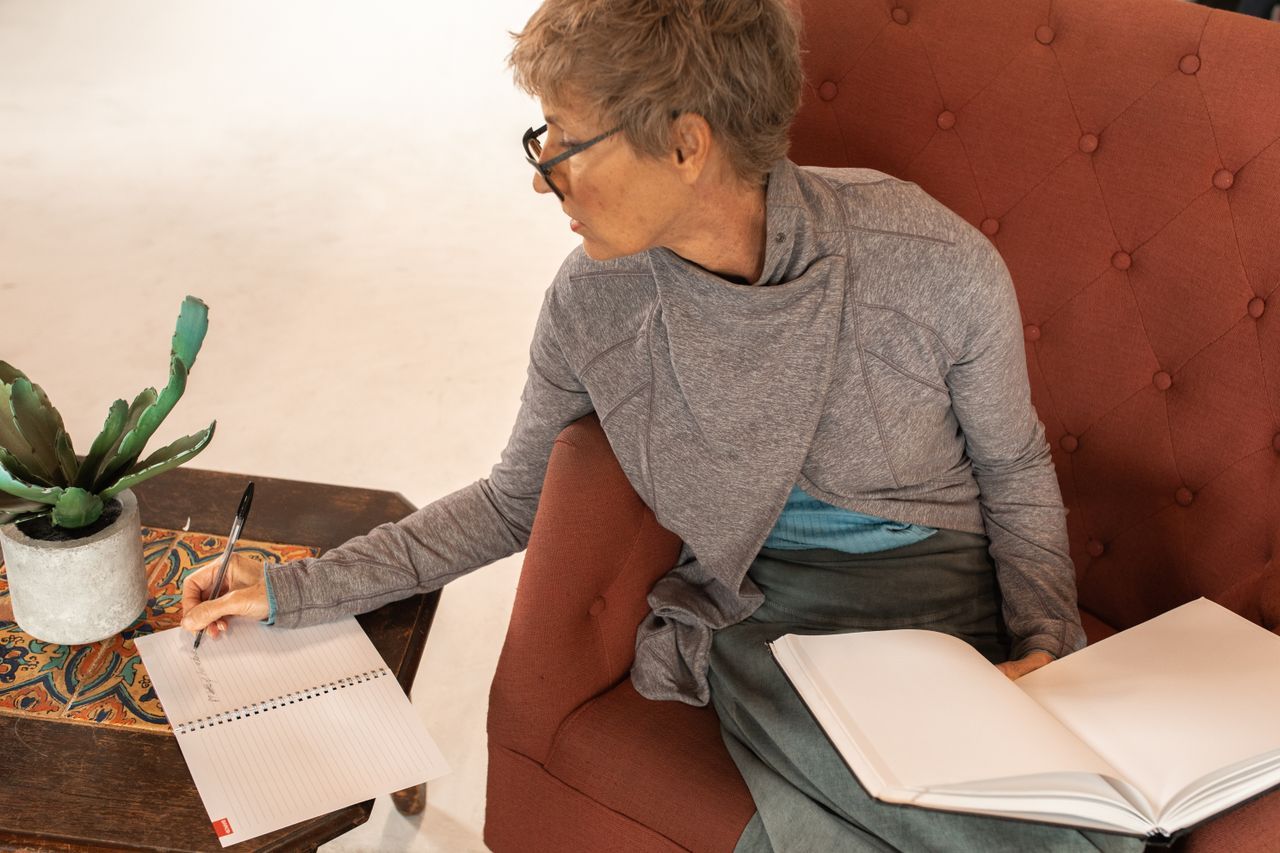 Senior woman in glasses writing notes in a notebook while seated indoors