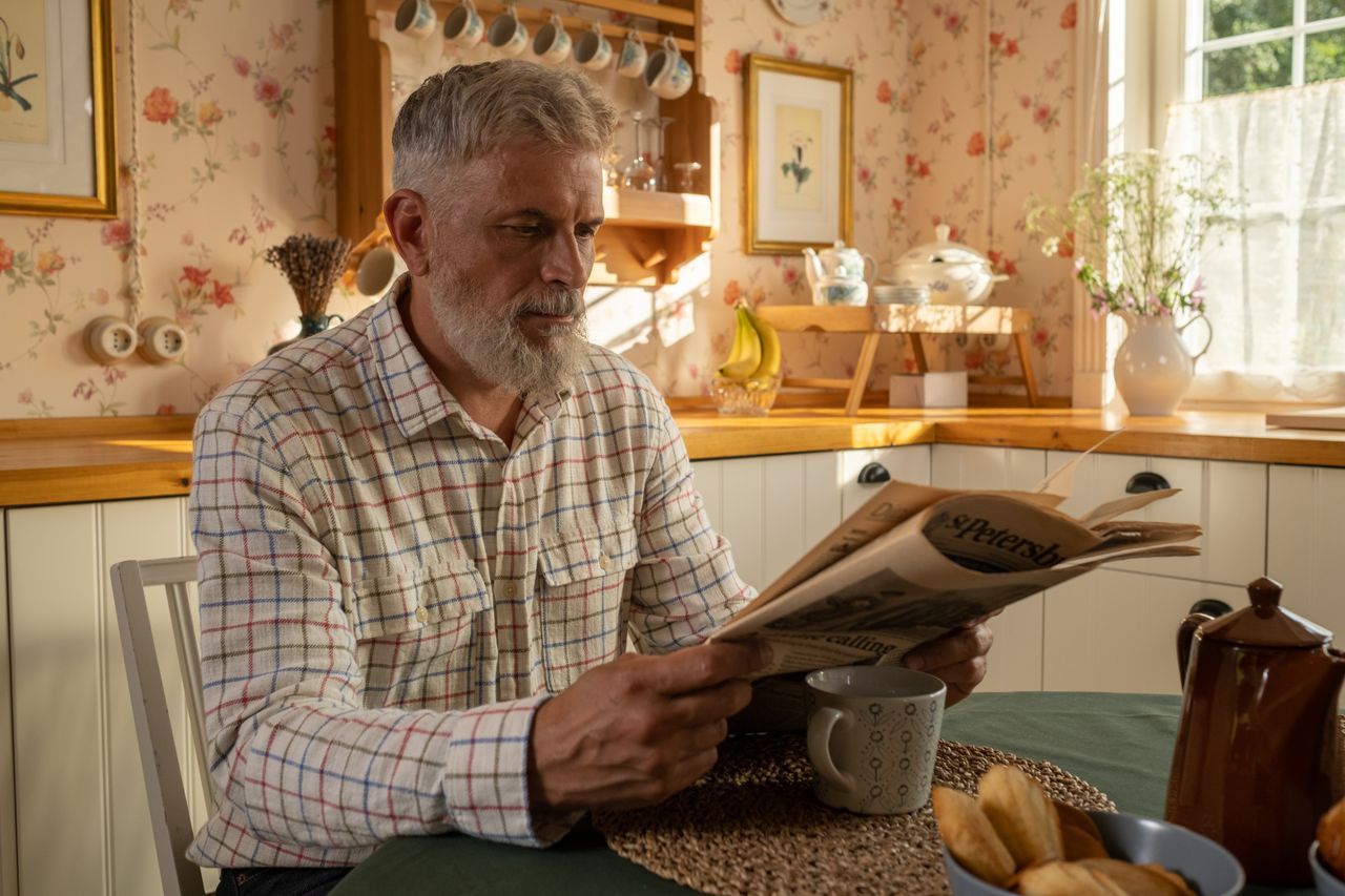 Senior man reading a newspaper at a kitchen table in warm morning light