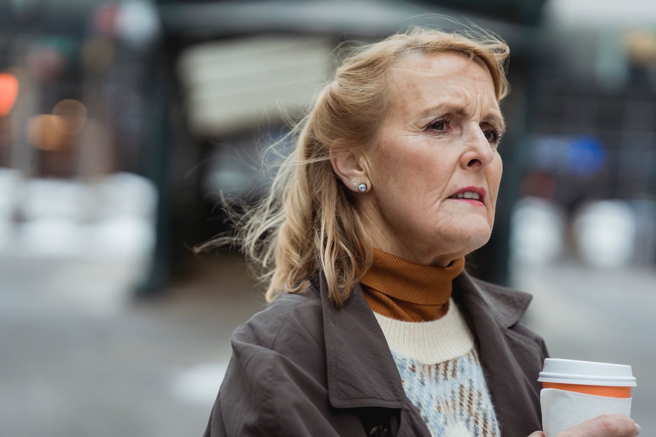 Senior woman with takeaway coffee looking out across a city street on a windy day