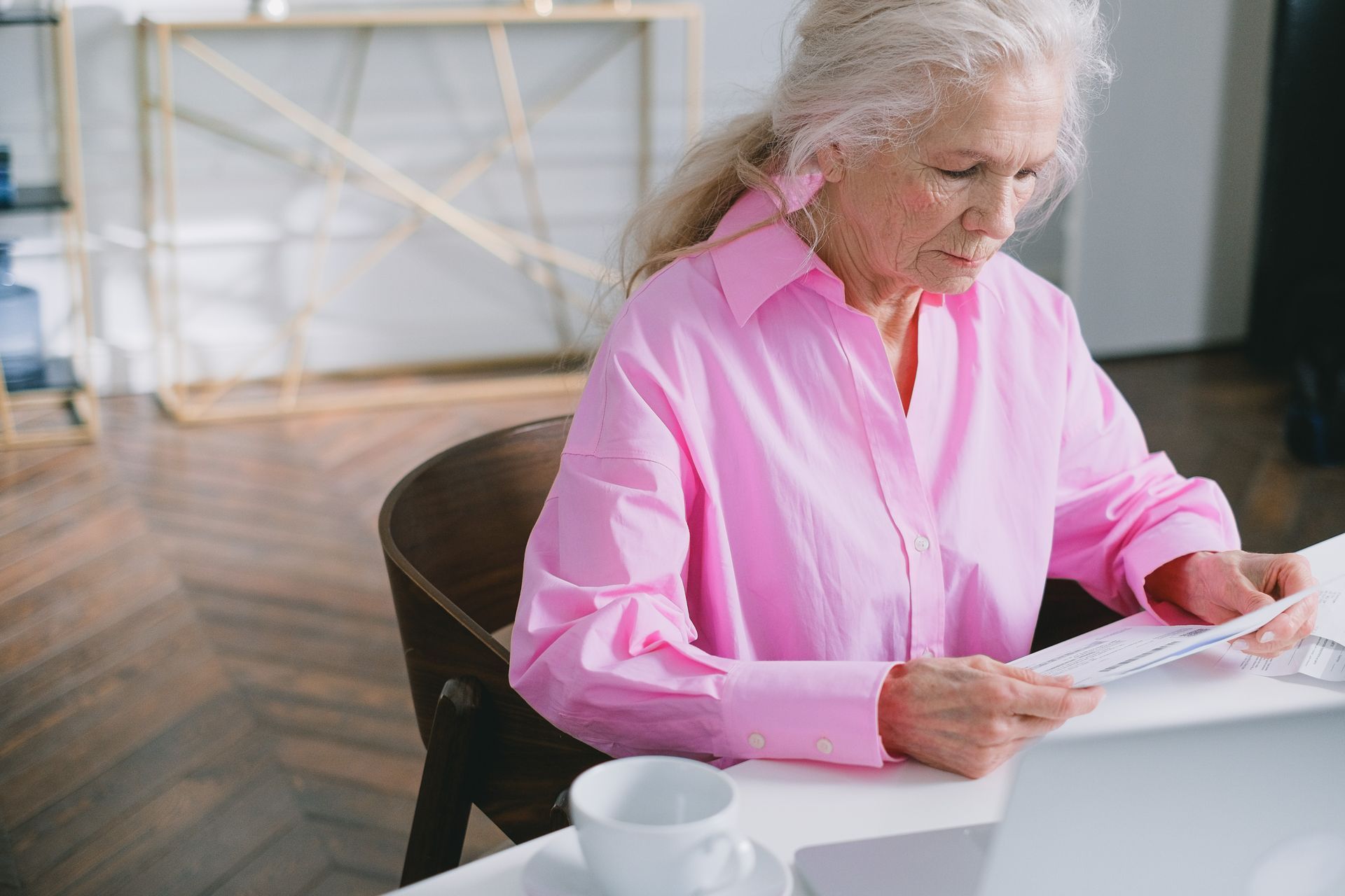Older woman with white hair and glasses reading papers at a home office desk