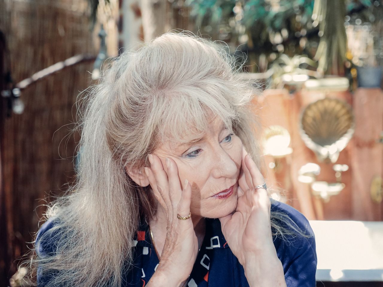 Grey-haired woman resting her face in her hands in quiet thought, outdoors in warm natural light