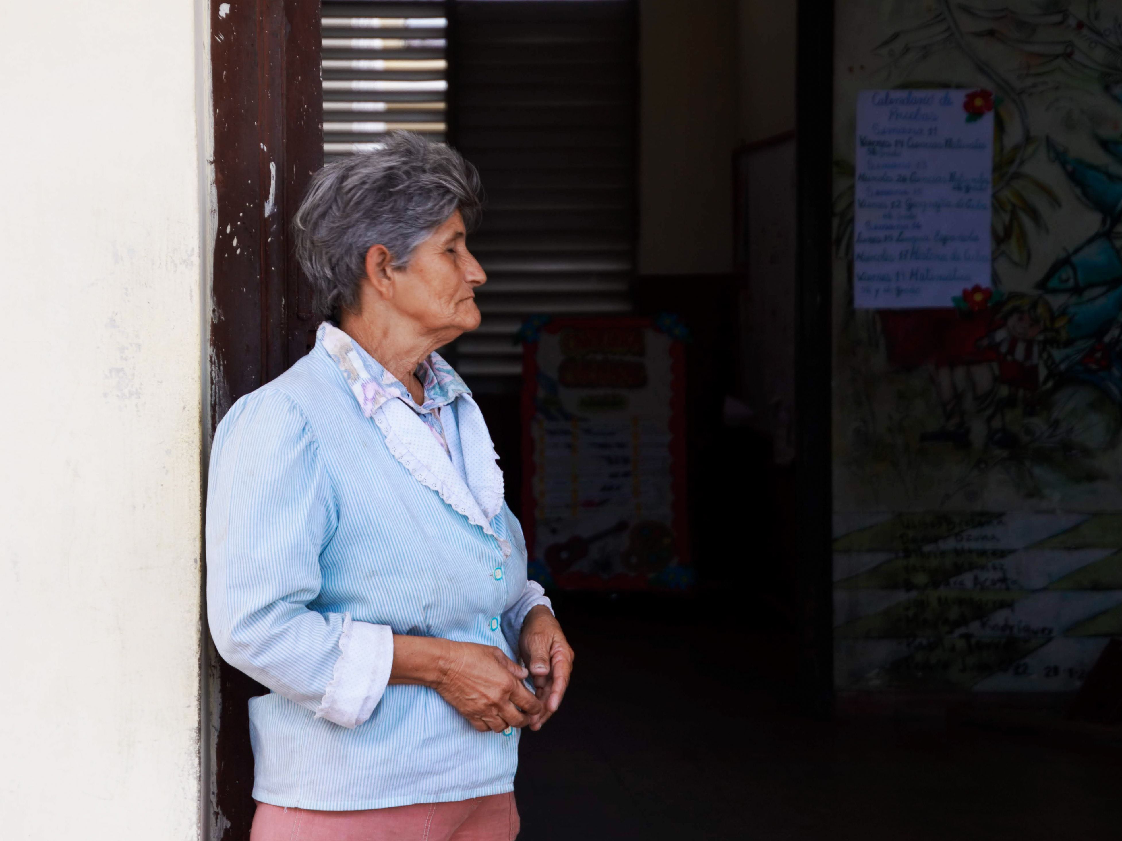 Grey-haired woman standing in a doorway looking outward in quiet thought with natural light on her face