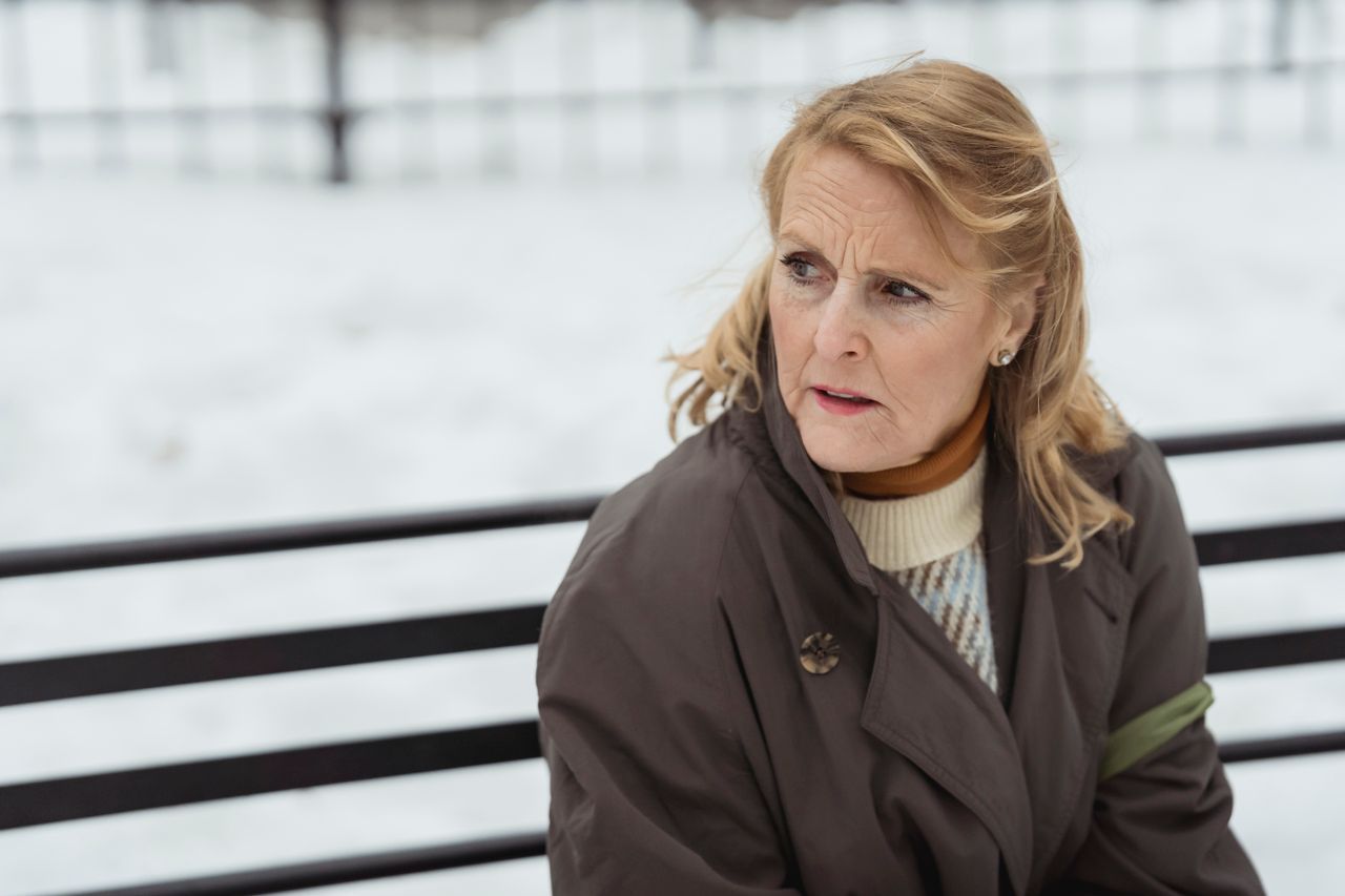 Contemplative older woman in a coat resting on an outdoor bench in winter, looking away in thought