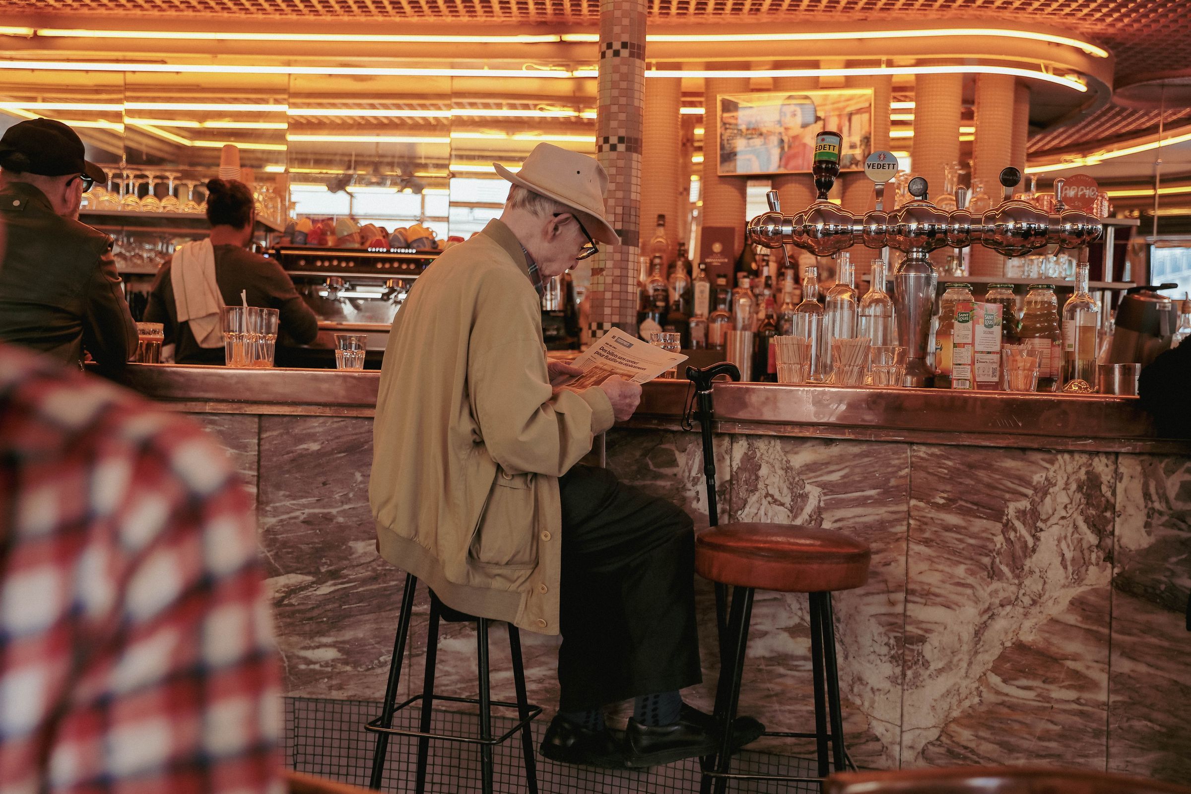 Senior man in a hat reading a newspaper at a bar counter indoors on a quiet morning