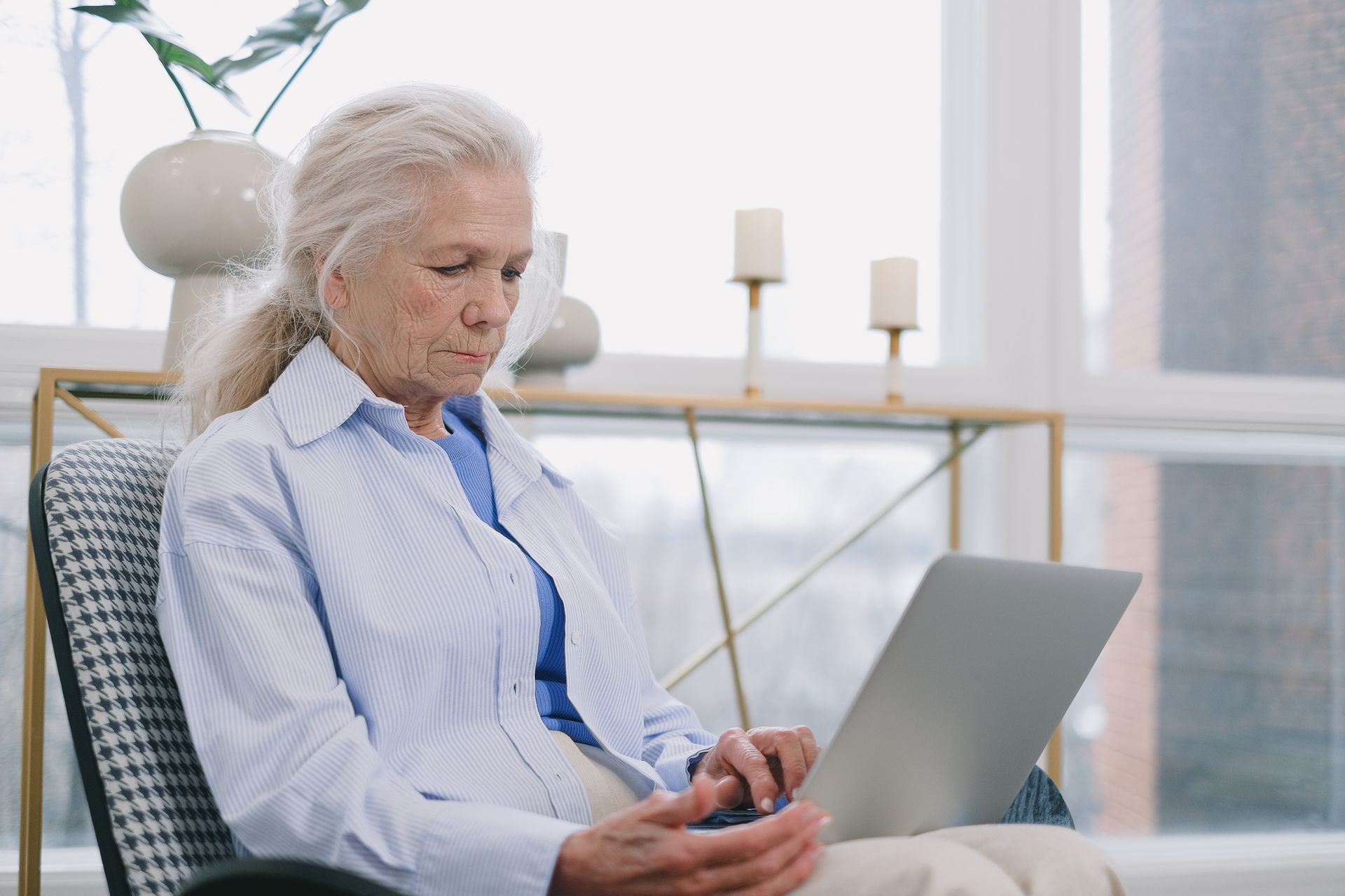 Senior woman with white hair using a laptop in a bright living room with natural light
