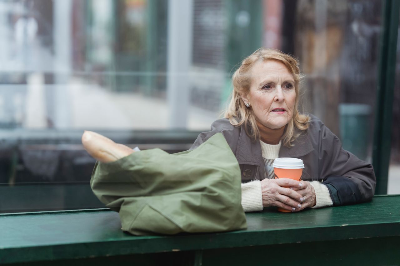 Contemplative older woman looking away at a cafe counter with a hot drink in hand