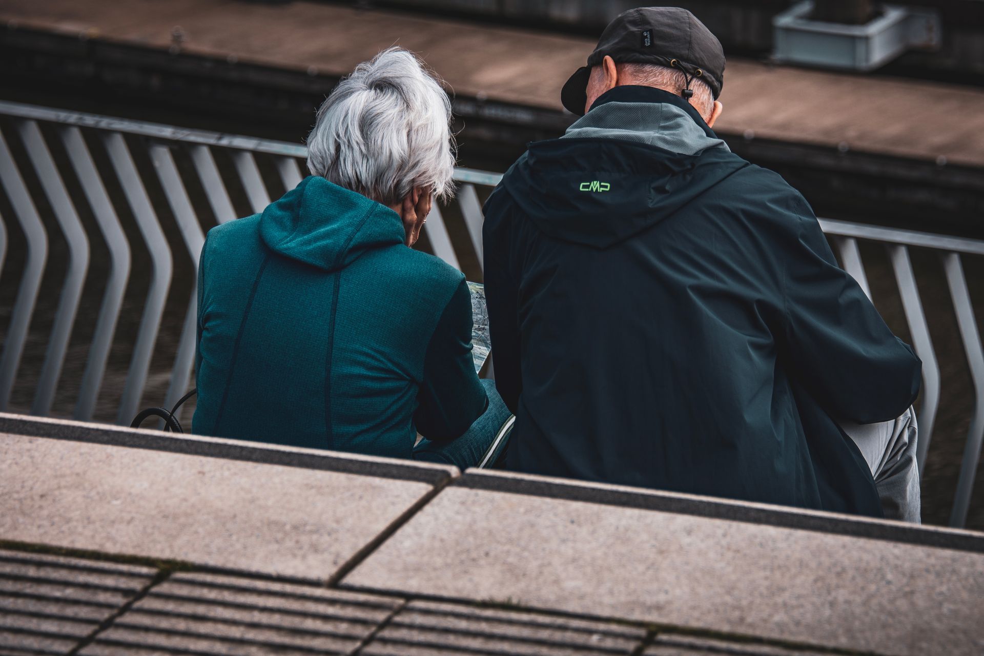 Older couple sitting together on stone steps overlooking a city, seen from behind