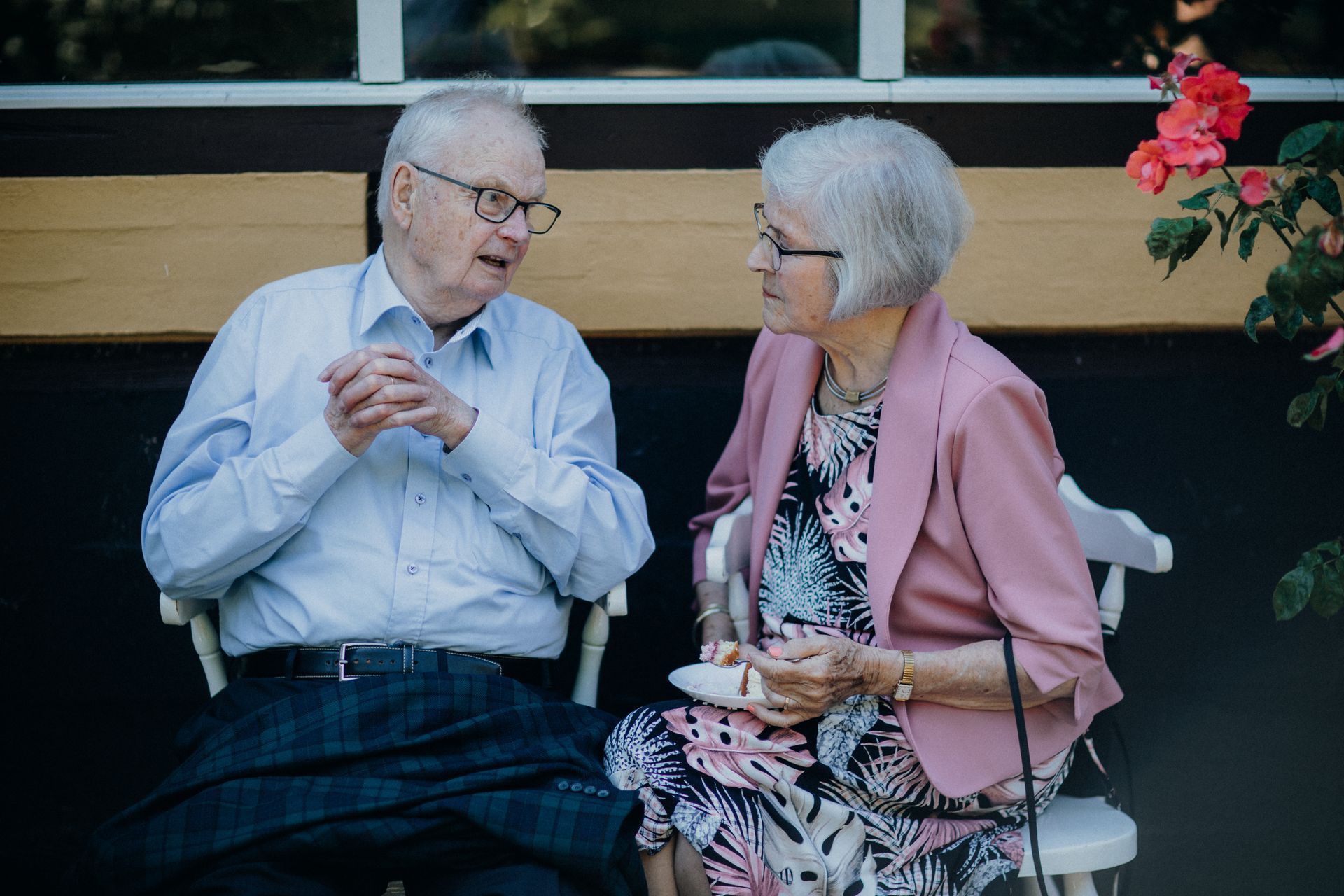 Senior couple sitting on separate chairs in a garden talking in natural daylight