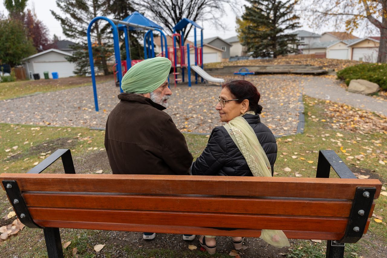 Older couple seen from behind on a park bench in autumn with fallen leaves