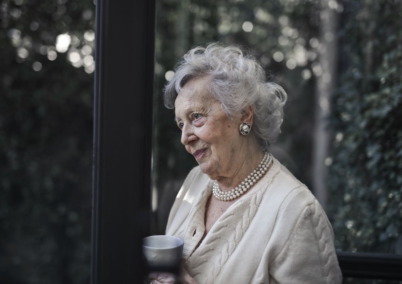 Senior woman with white hair holding a mug by a window in soft natural light