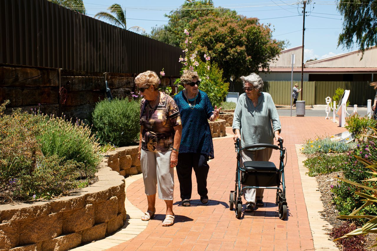 Three senior women walking and chatting together along a sunny garden path