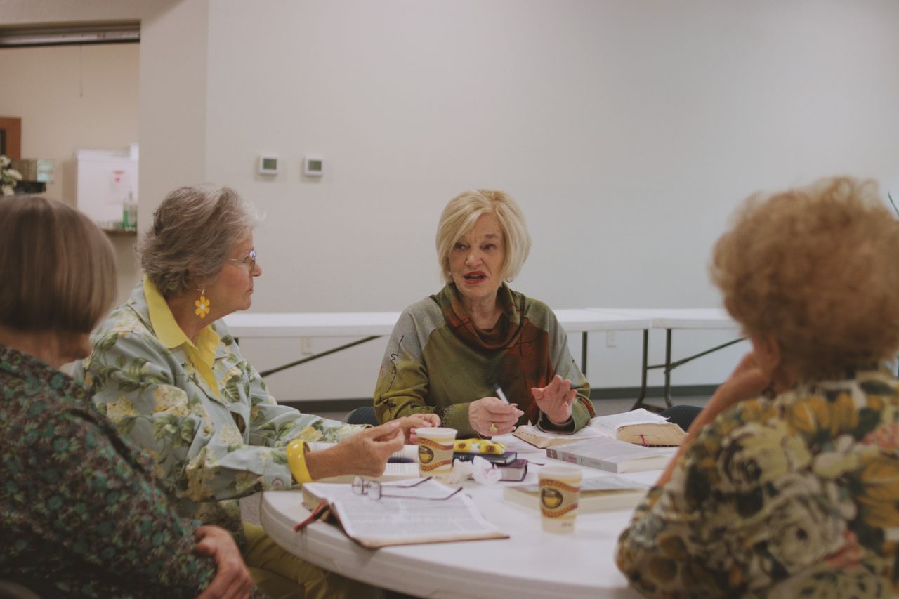 Women over 50 seated around a table at a community group meeting with notebooks and cups