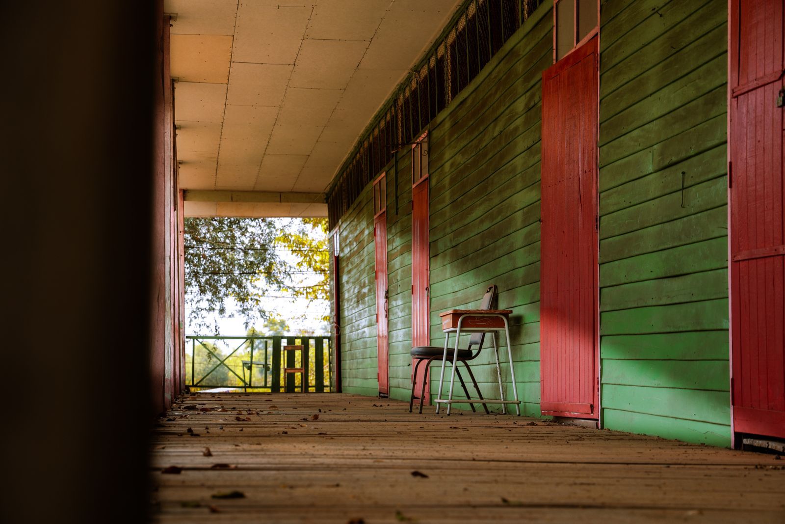A rustic porch with empty chairs and autumn leaves scattered on the wooden floor in quiet morning light