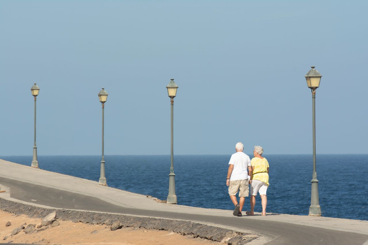 Older couple with white hair walking together on a seaside promenade, seen from behind