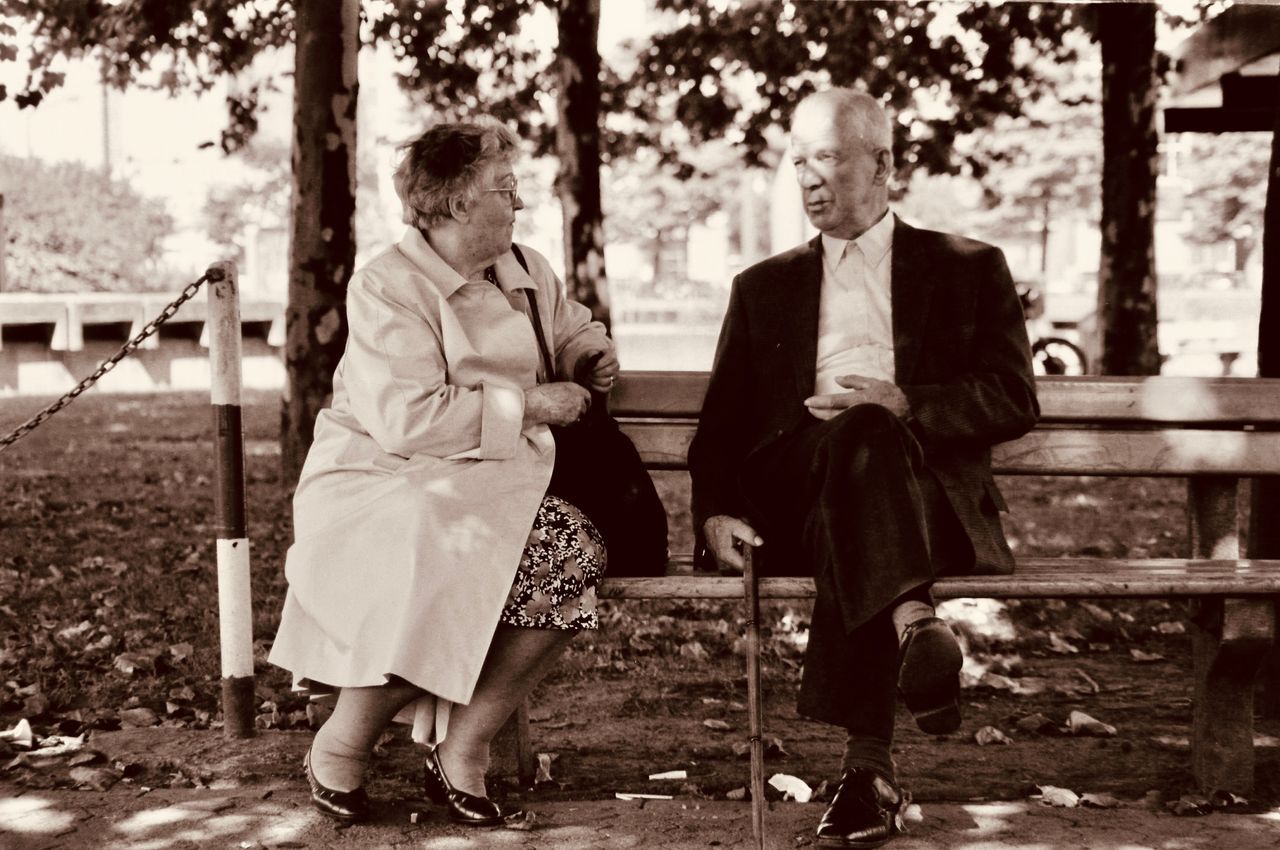 Older woman and man in conversation on a park bench among autumn trees