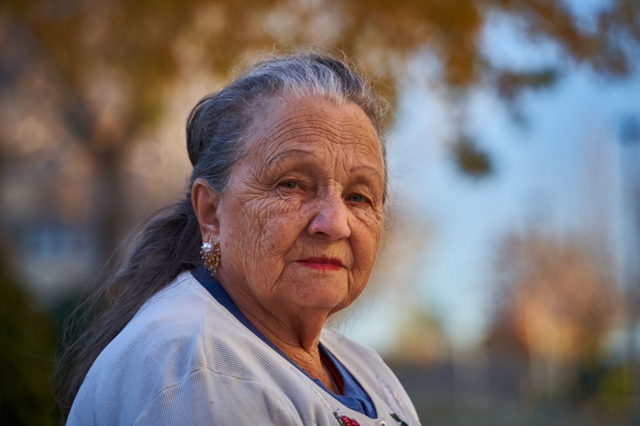 Older woman with grey hair outdoors in golden-hour light, expression calm and composed