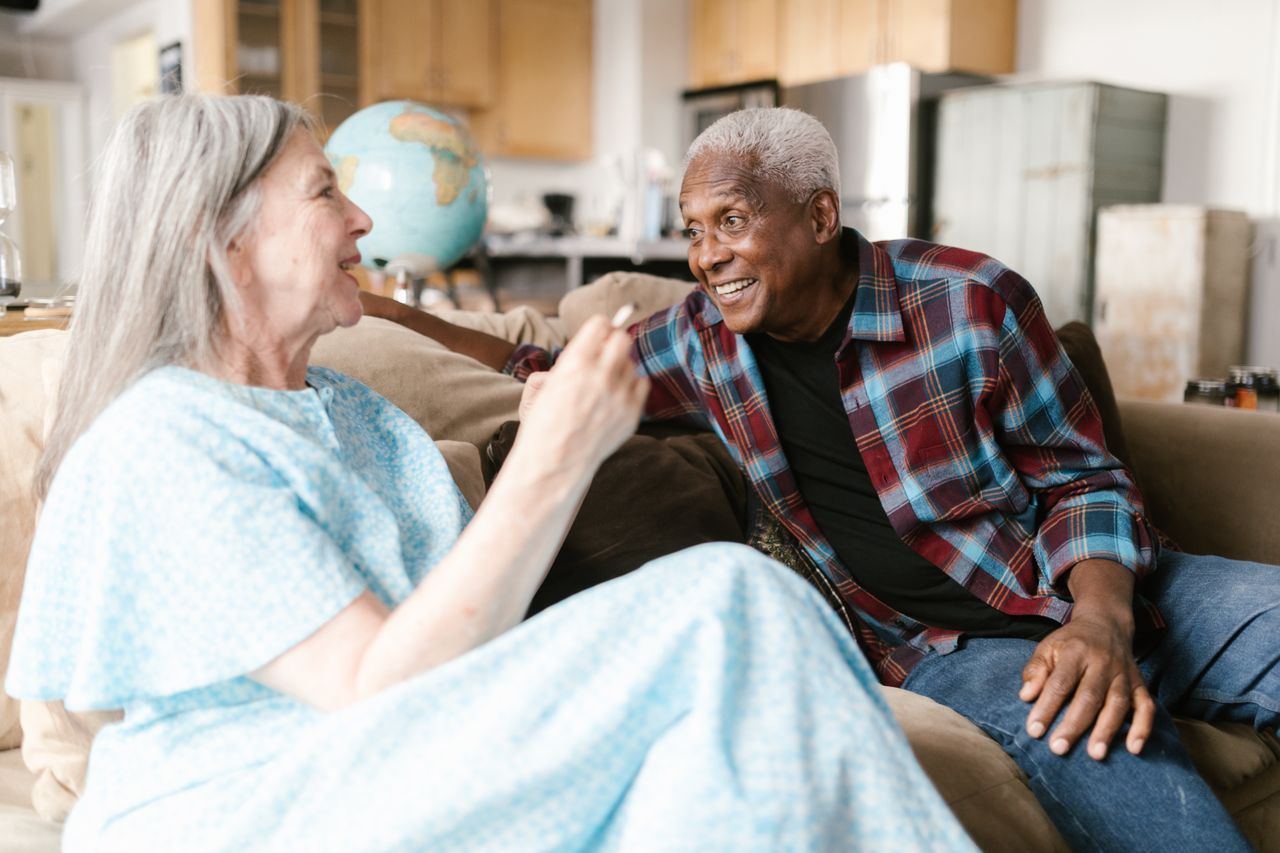 Couple over 50 sitting together on a sofa in soft morning light mid-conversation