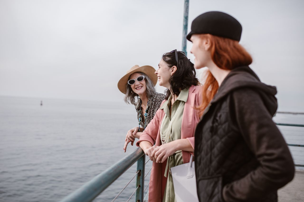 Three senior women laughing together by the sea on a sunny day