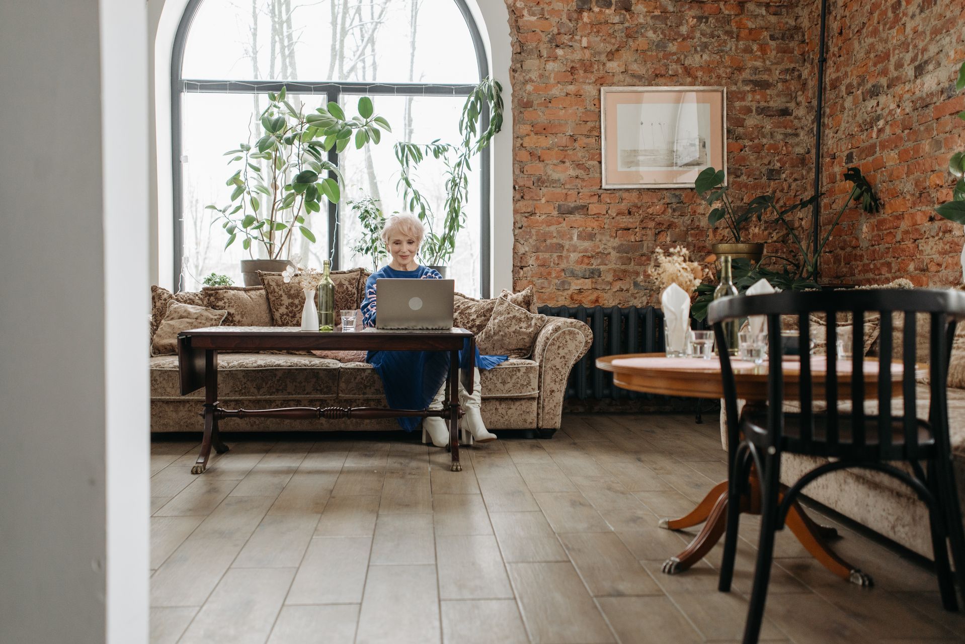 Older woman with white hair working on a laptop in a sunlit living room