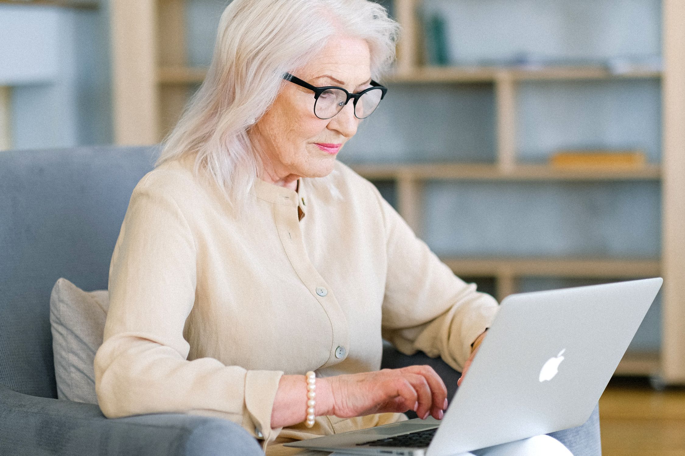 Woman with white hair and glasses using a laptop in an armchair at home