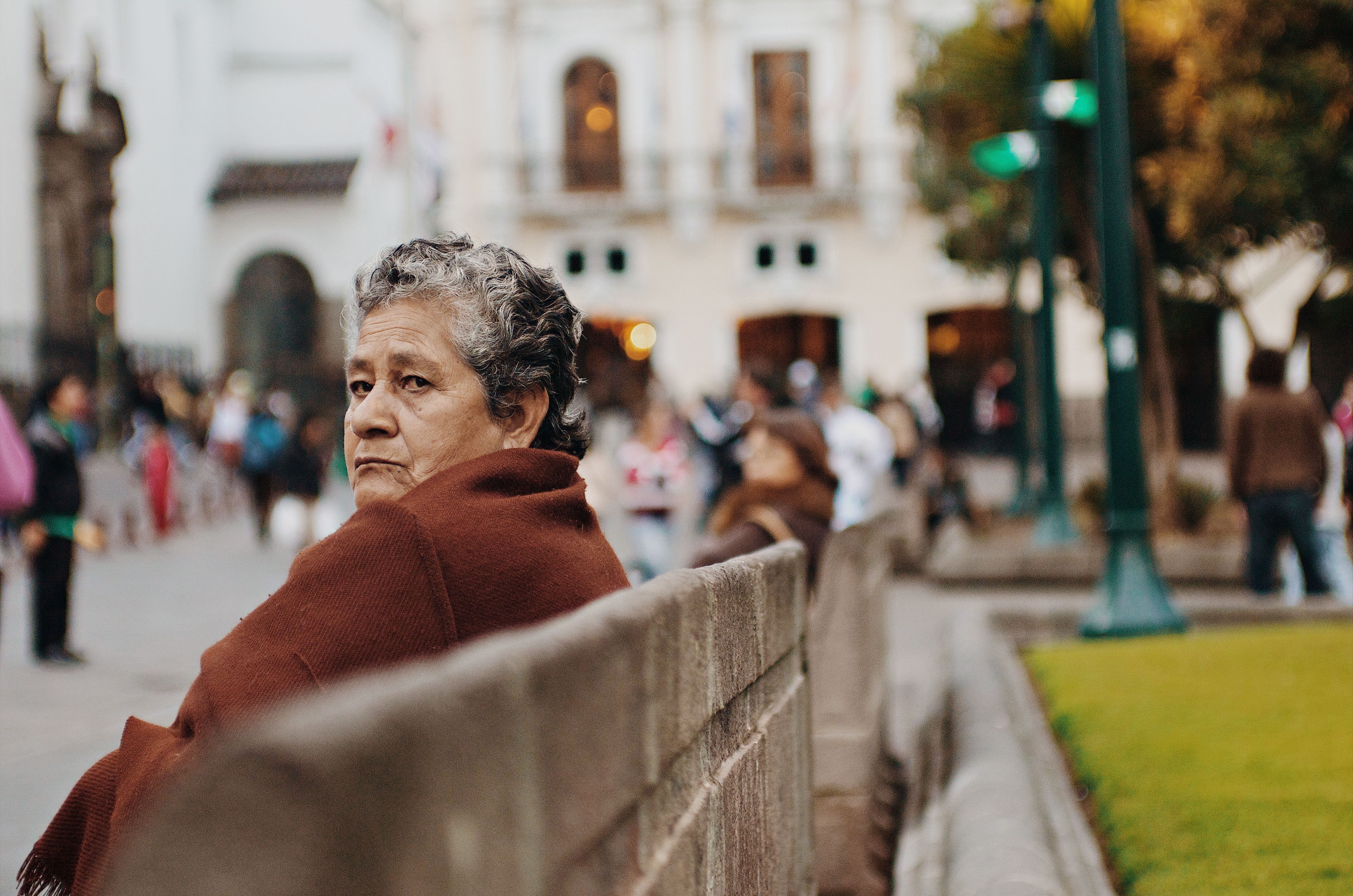 Senior woman with grey hair in a rust shawl looking pensively across a public square