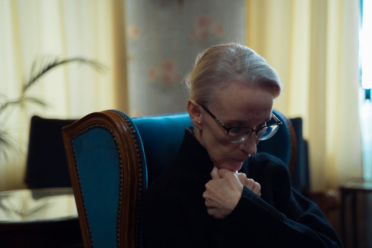 Elderly woman wearing glasses sitting in an armchair lost in thought in a warmly lit room