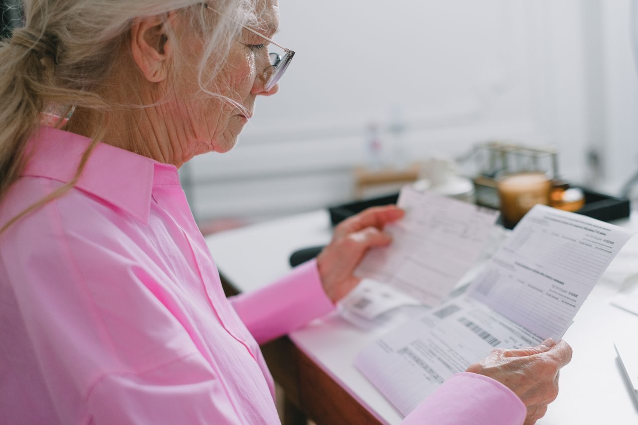Senior woman in glasses and pink shirt reviewing paperwork at a home desk