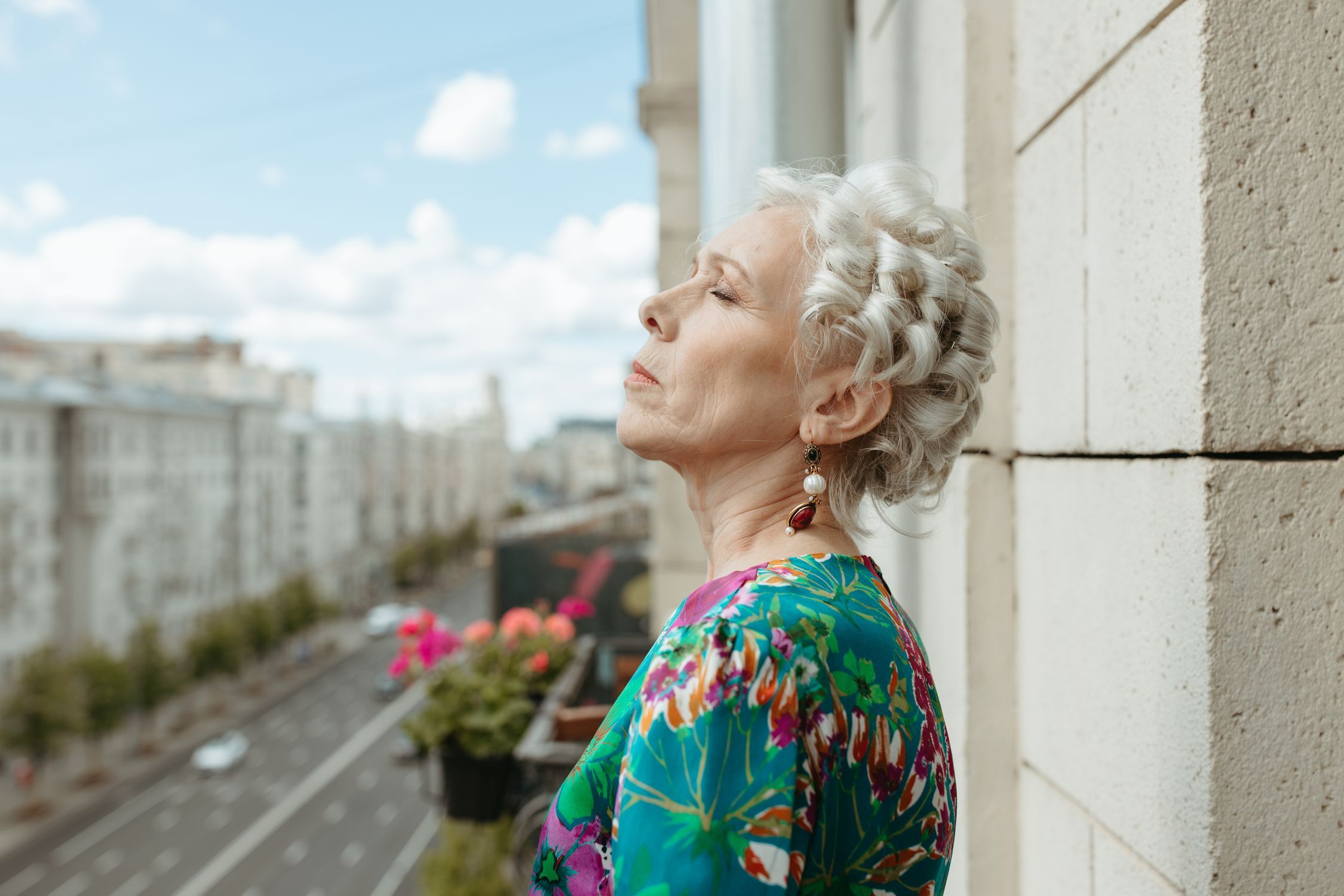 Senior woman with white hair enjoying a calm moment on a balcony overlooking a city