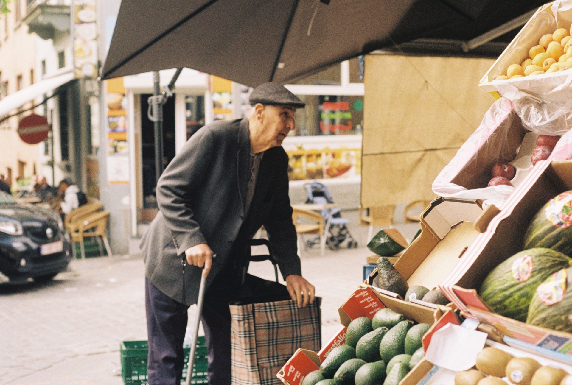 Elderly man with a cane browsing fresh produce at an outdoor market stall