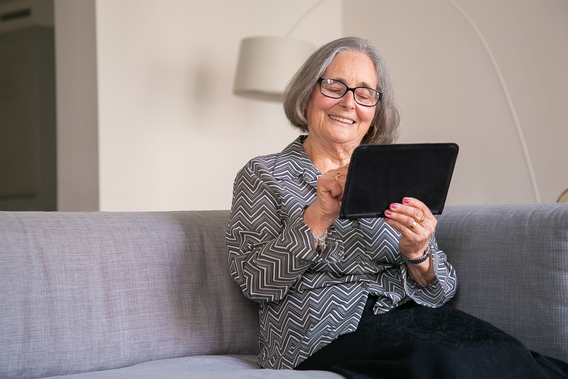 Woman with grey hair using a tablet on a comfortable sofa at home