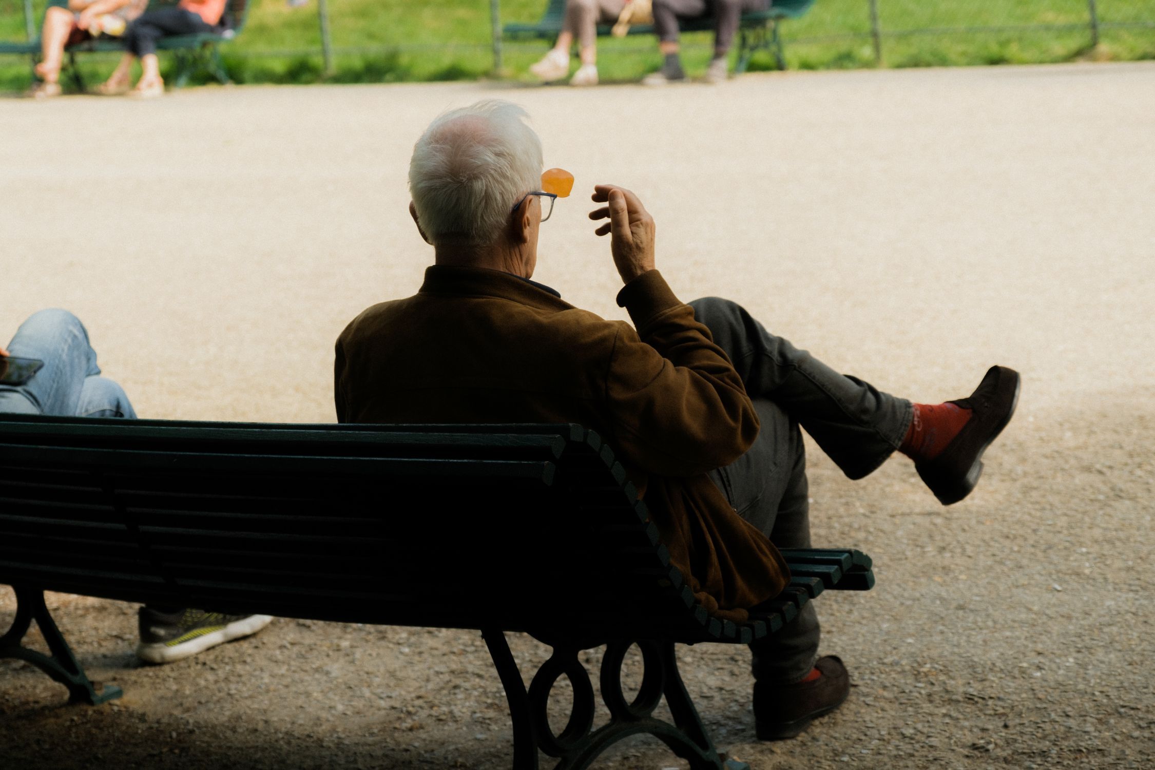 Senior man with grey hair sitting alone on a park bench on a sunny day