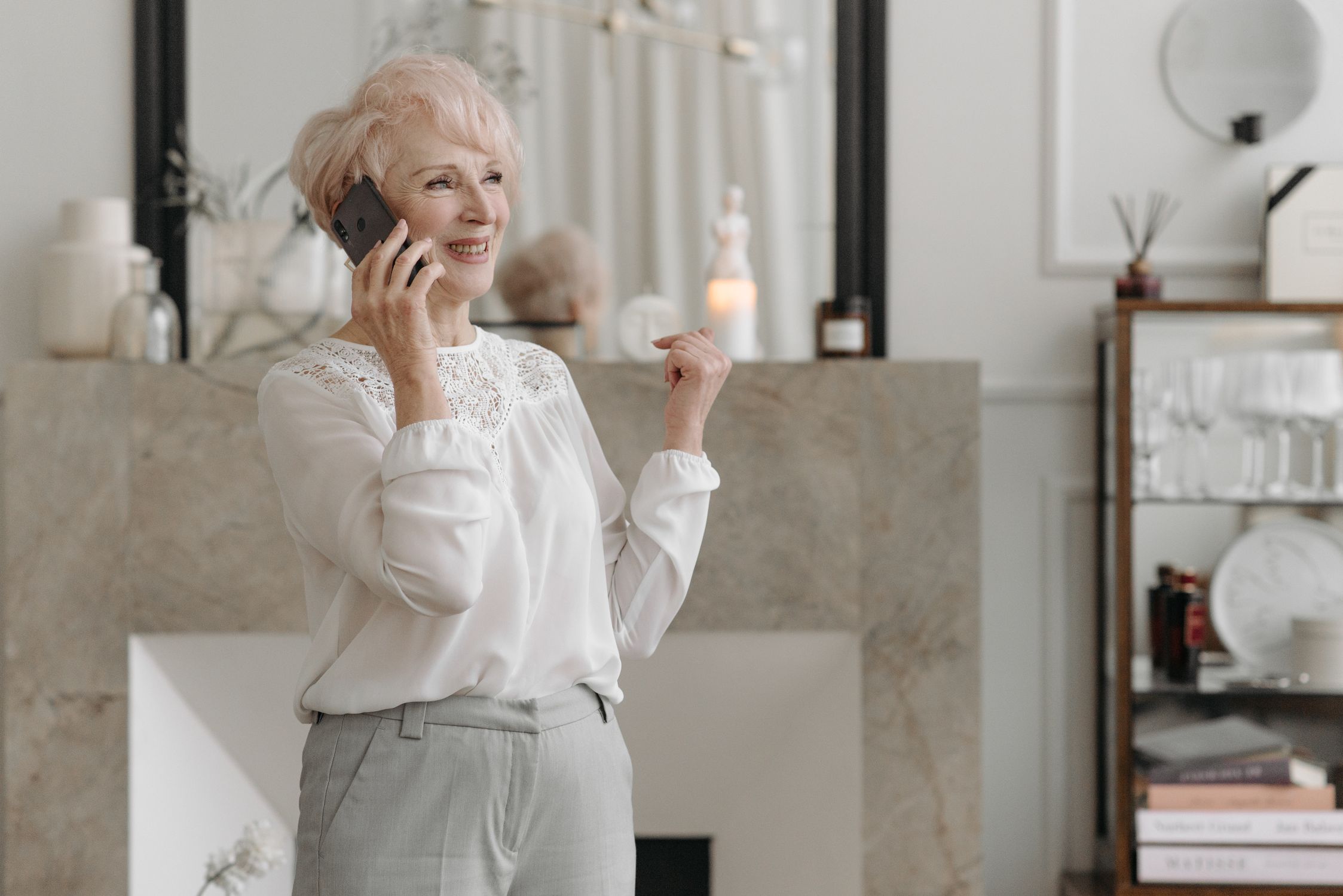 Woman over 65 with grey hair talking on phone in a bright living room