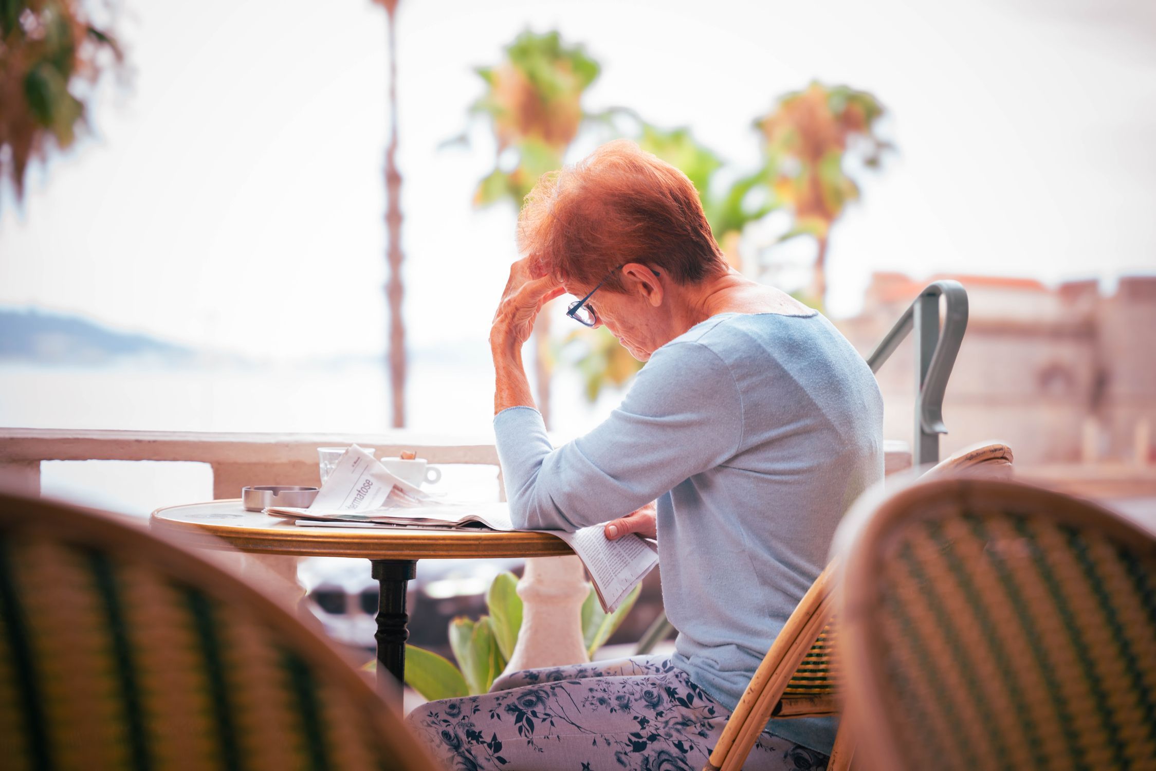 Elderly woman enjoying a serene morning at a seaside cafe with soft natural light