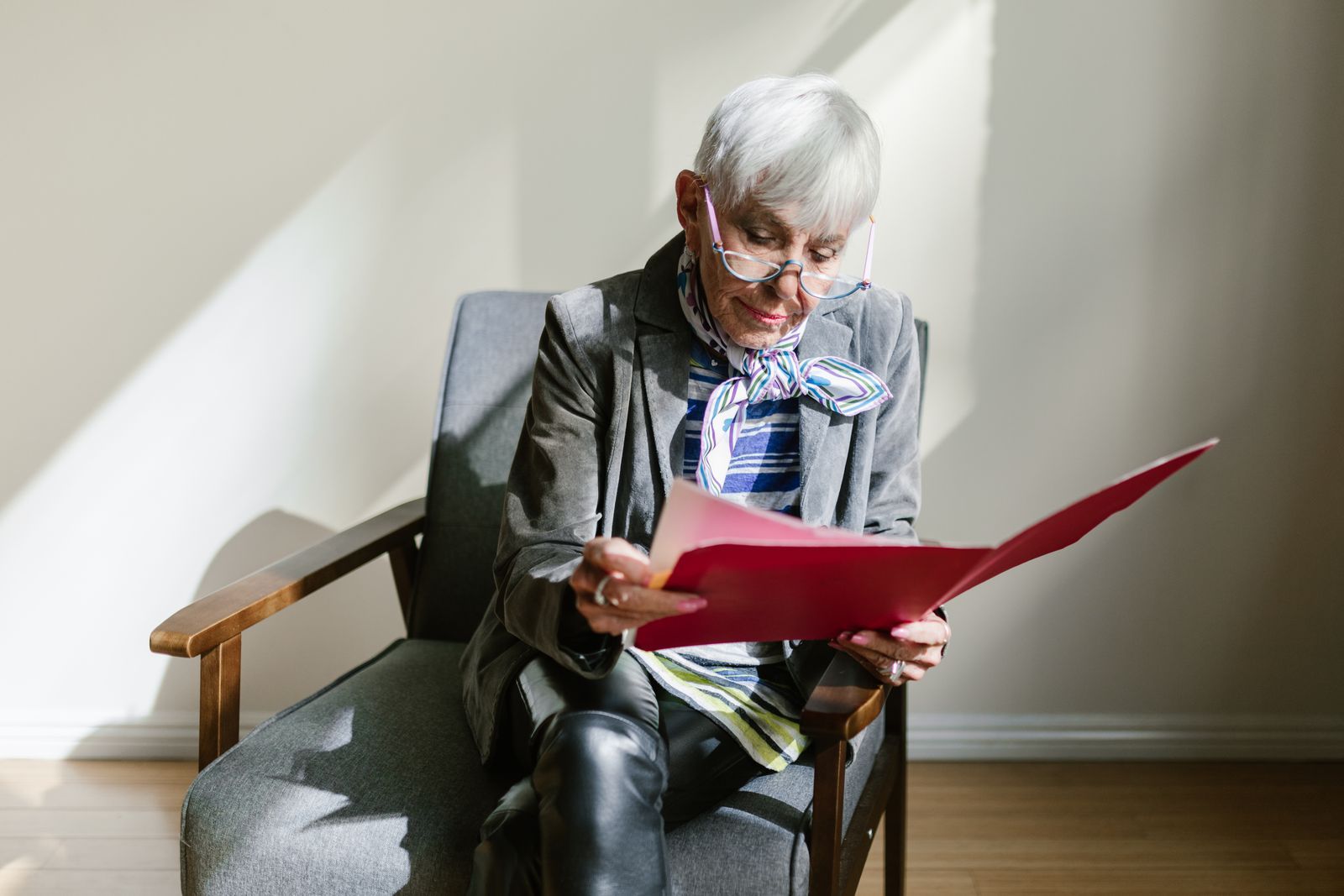 Senior woman with glasses reading a document in an armchair by natural side light