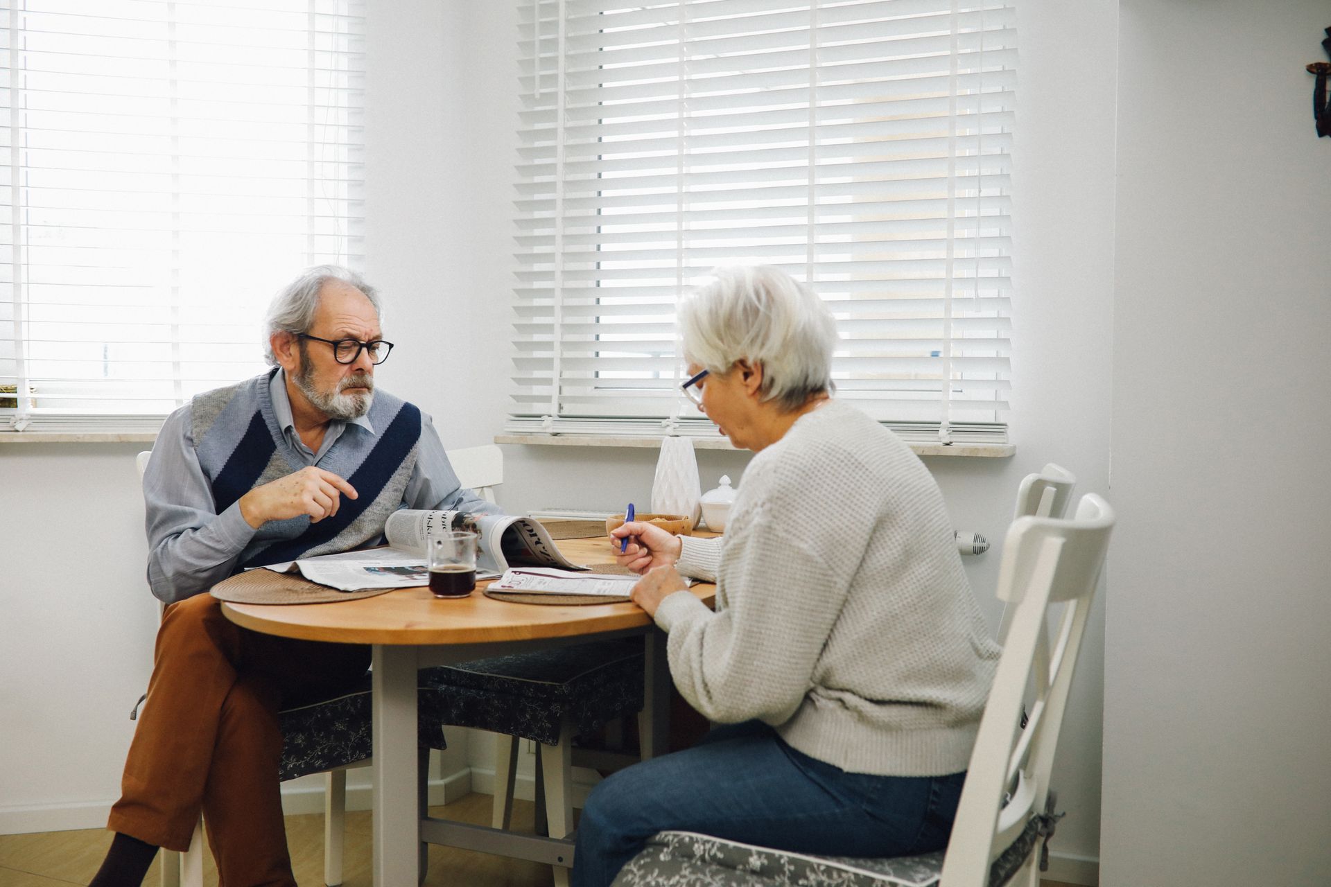 Older couple reading newspapers over coffee together at a bright dining table