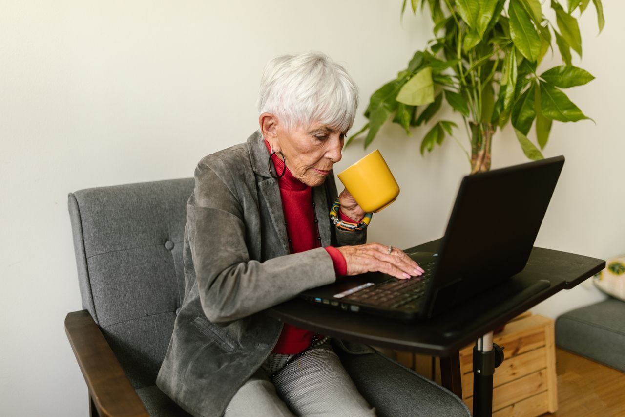Silver-haired woman focused on her laptop at home with a coffee mug in hand