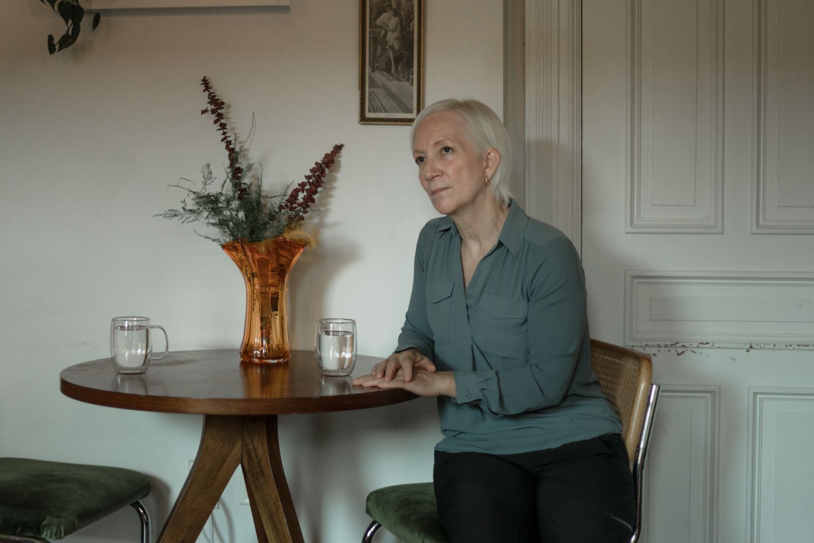 Senior woman with white hair sitting alone at a small table with glasses of water in a peaceful room