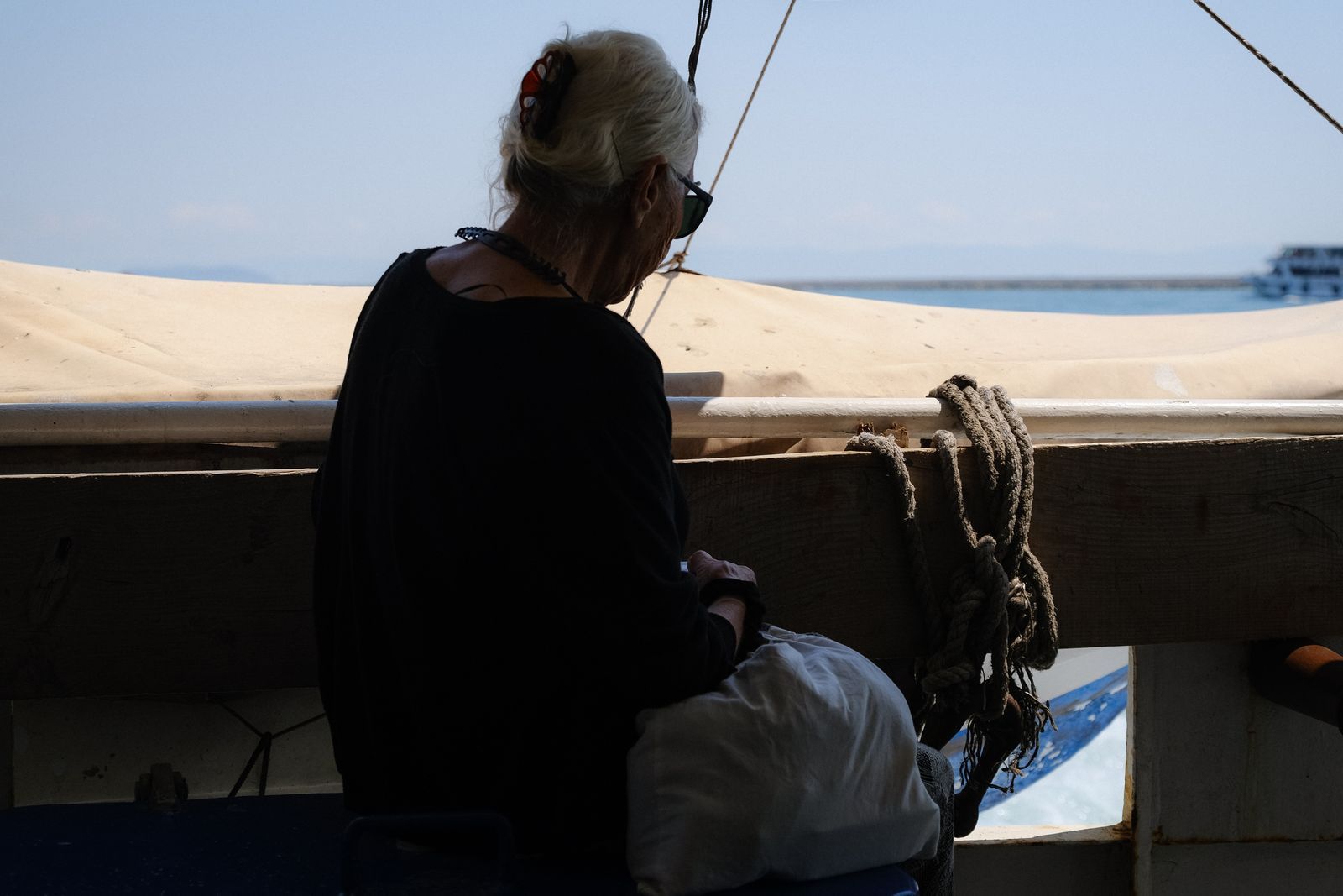 Gray-haired woman sitting on a boat looking out toward the sea on a sunny day