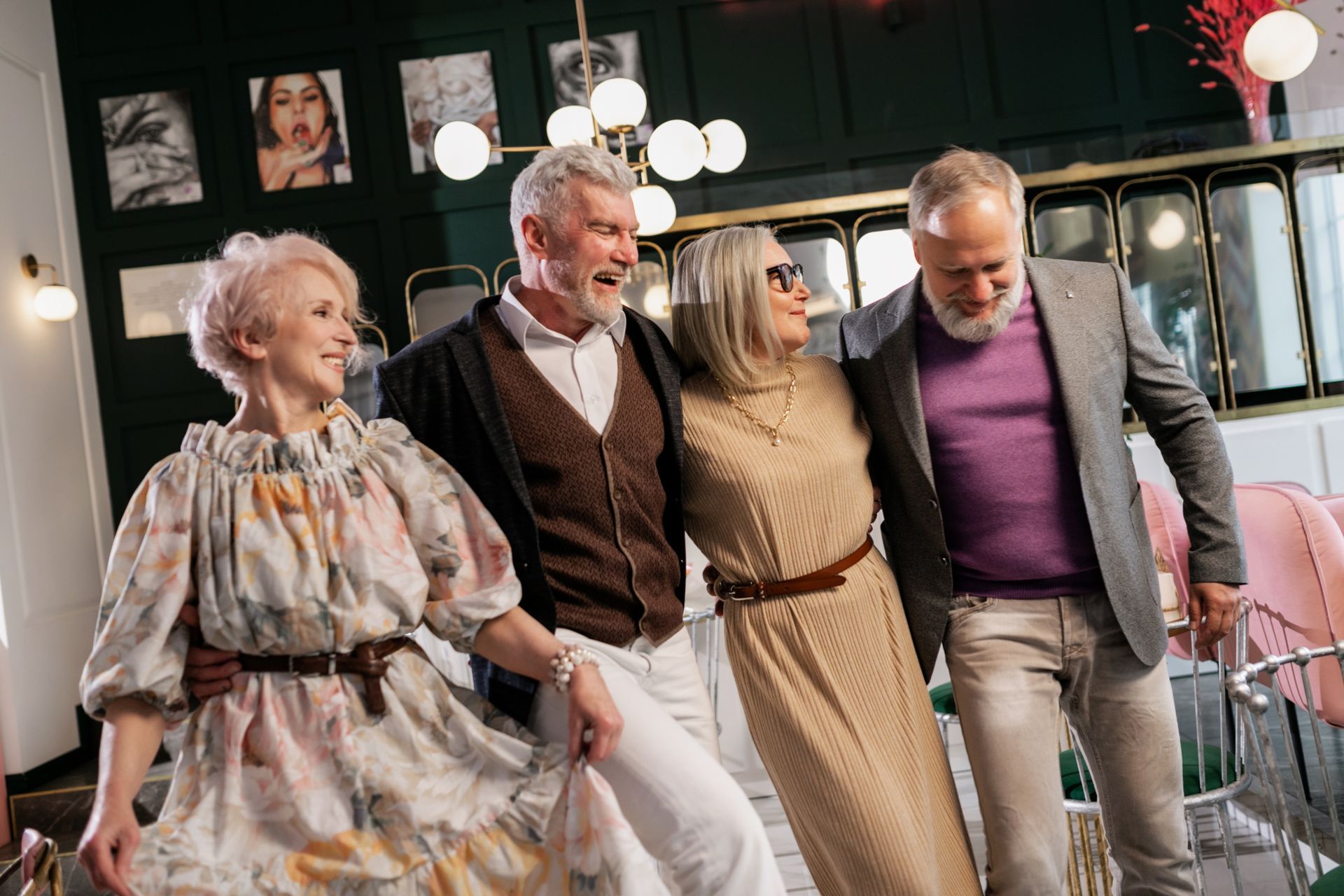 Four well-dressed adults over 50 standing together laughing at a stylish indoor social gathering