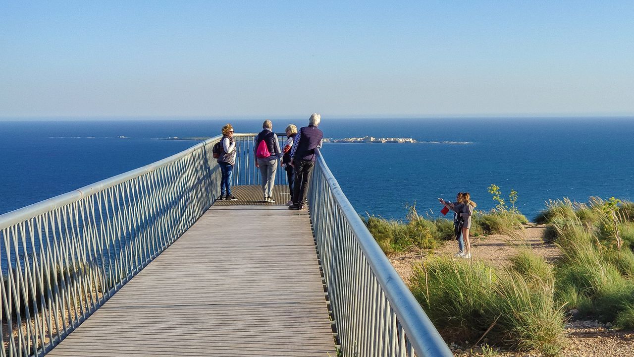 Group of people enjoying ocean views from a clifftop walkway on a sunny day