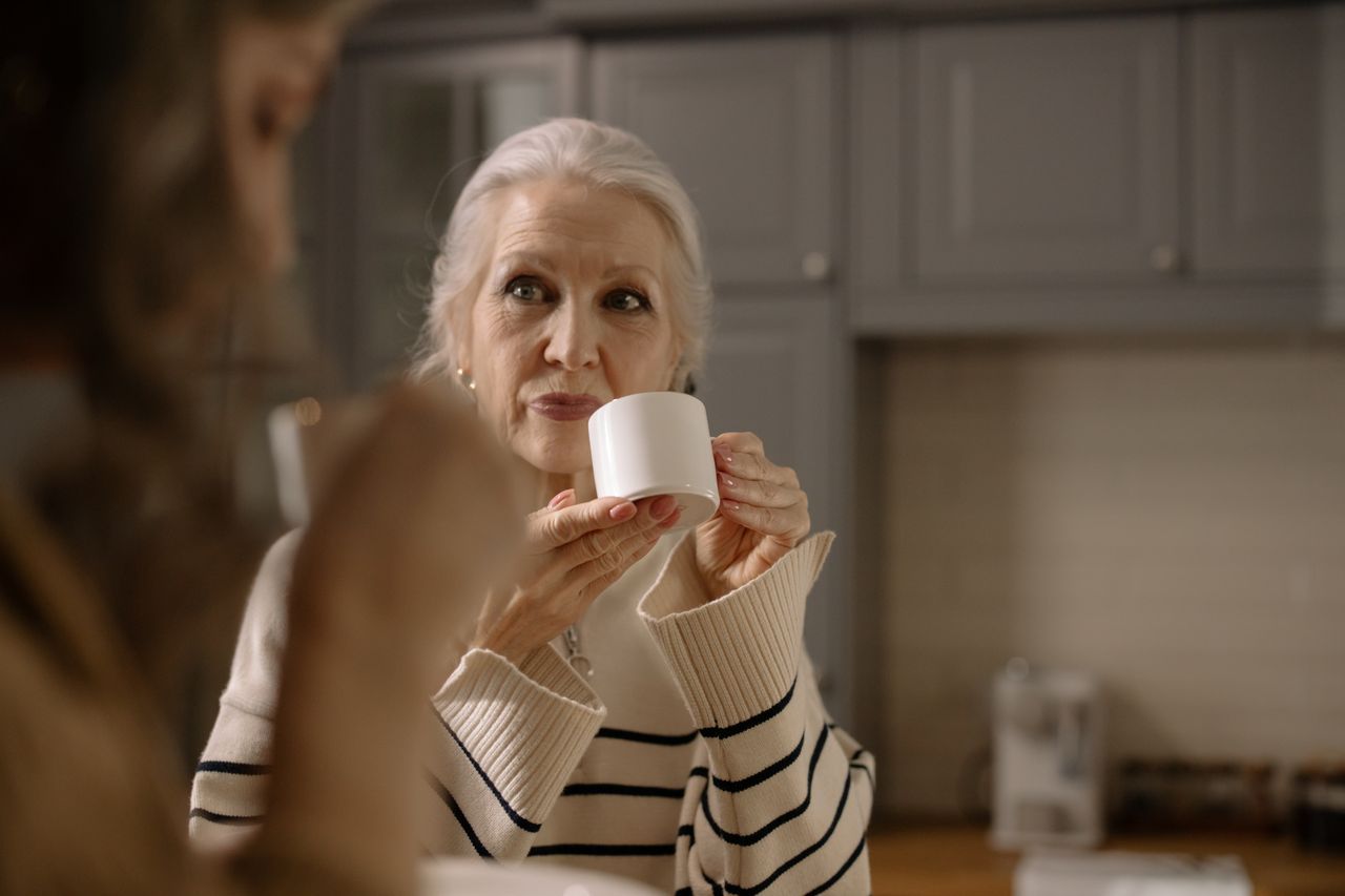 Senior woman in striped sweater holding a ceramic cup indoors in soft natural light