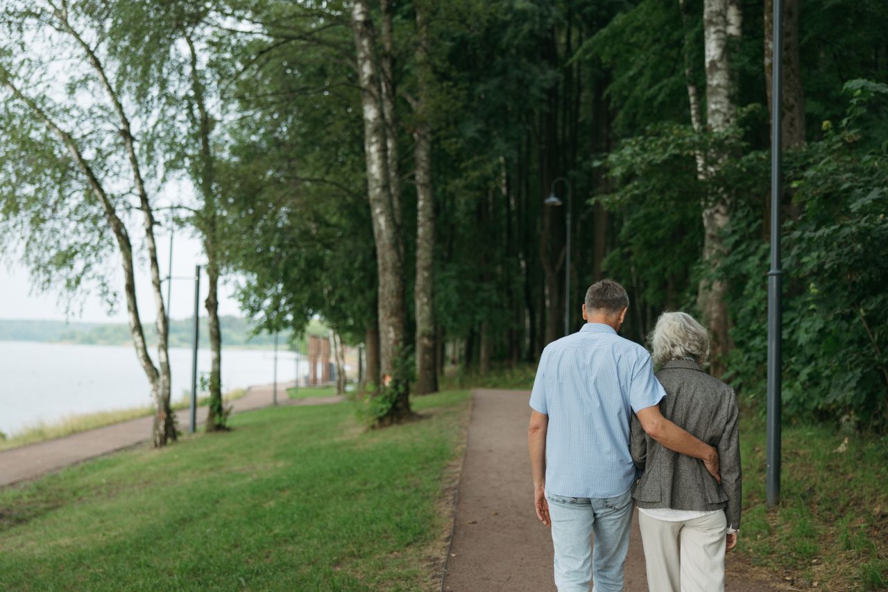 Two people over 50 walking close together on a quiet tree-lined path at dusk