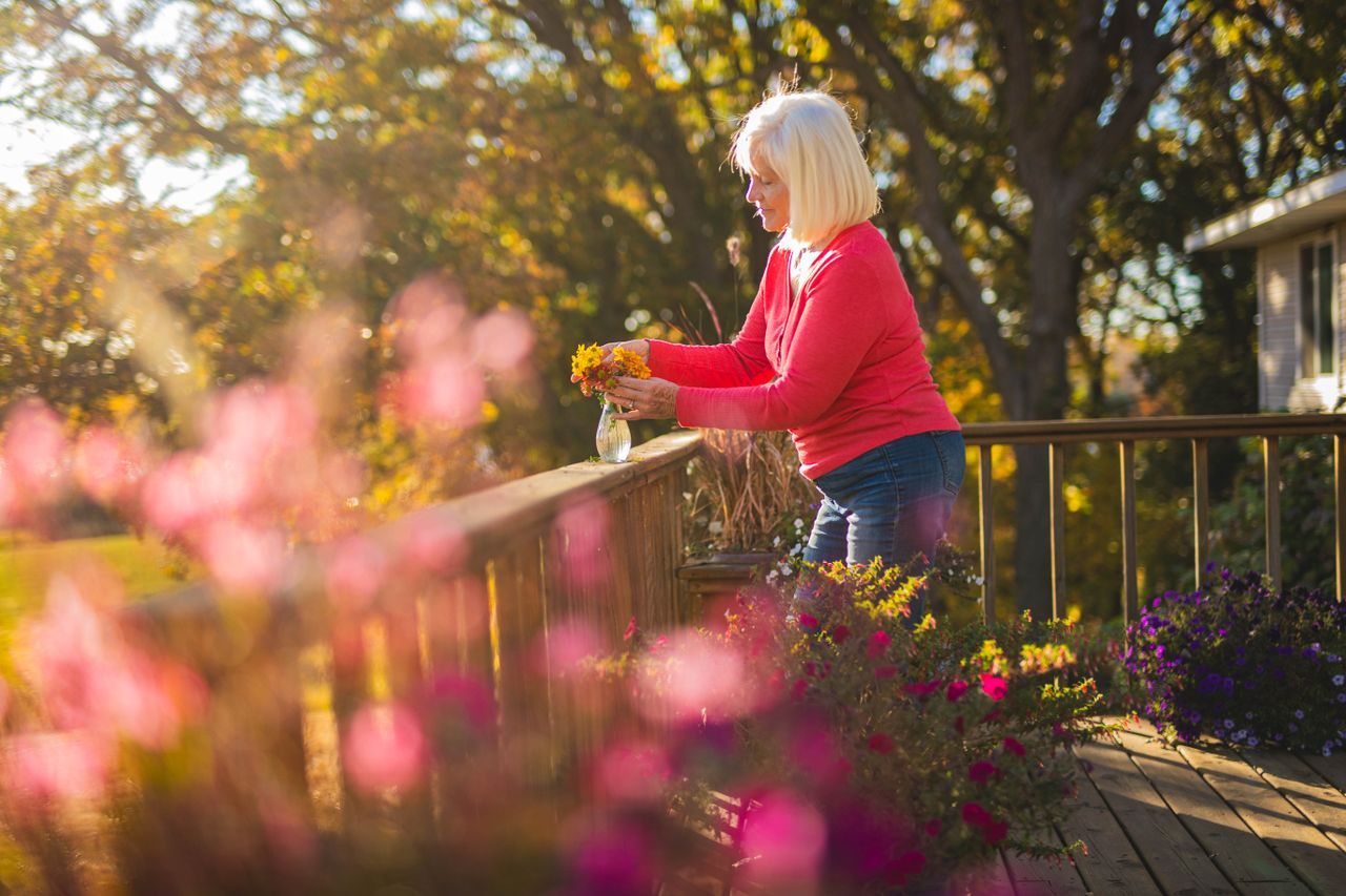 Older woman arranging flowers on a wooden deck in warm autumn light